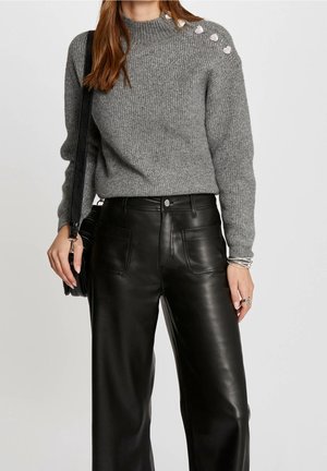 Grijze gebreide trui met een geribbelde textuur en metallic draad, met decoratieve zilveren knopen op de schouder, gecombineerd met zwarte leren broek.