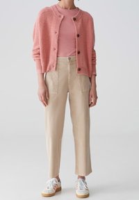 Světle růžový kardigan z vlněné směsi s kulatým výstřihem a zapínáním na knoflíky, doplněný o přiléhavé růžové tričko a béžové rovné kalhoty. Bílé tenisky.