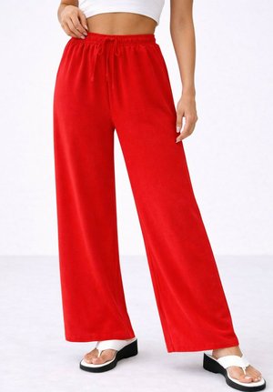 Femme portant un pantalon rouge taille haute à jambes larges avec un cordon, un top court blanc et des sandales compensées blanches laissant apparaître les pieds nus.