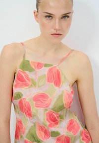 Bloemenjurk met roze en groene bladenpatronen, gemaakt van lichtgewicht stof, met dunne bandjes en een ontspannen pasvorm.