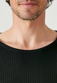 Zwarte geribbelde shirt met een brede, ronde halslijn, die een gladde textuur en minimale stiksels laat zien. Huid zichtbaar in het halsgebied.
