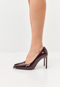 Décolleté in pelle lucida bordeaux con punta affusolata, design elegante, tacco a stiletto di 10 cm e lievi accenti argentati.