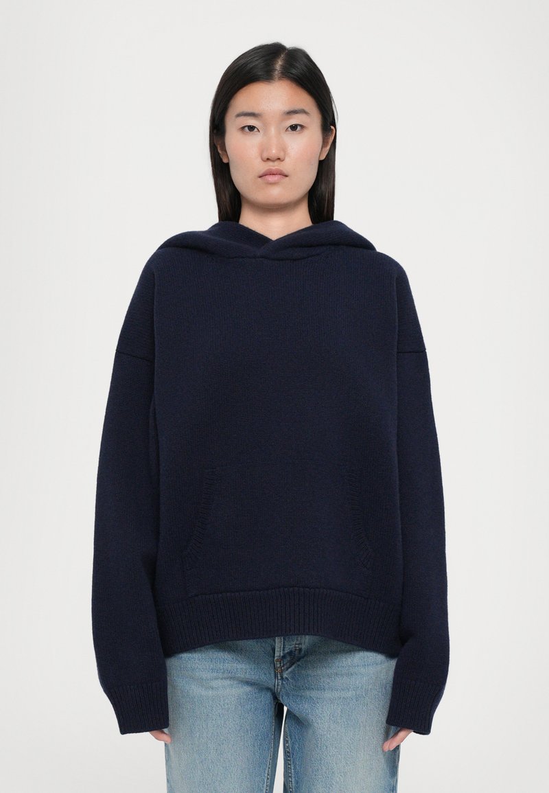 Navy blue hooded sweatshirt with a loose fit, ribbed cuffs, and hem. Features two front pockets and soft knit texture.