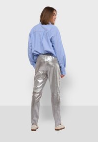 Světlomodrá pruhovaná košile s dlouhými rukávy, zastrčená do lesklých stříbrných kalhot s úzkým střihem a elastickým pasem, doplněná béžovými botami.