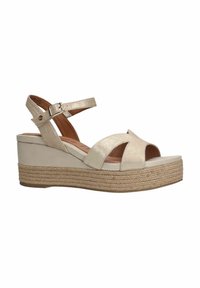 Beige wedge sandalen met een metallic afwerking, voorzien van kruislingse banden en een jute-wrapped platformzool. Inclusief verstelbare enkelriem.