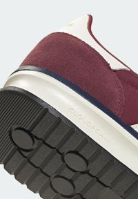 Gros plan sur le talon d'une basket montrant du daim bordeaux, une semelle intermédiaire blanche avec le texte "CLOUDFOAM", et une semelle extérieure en caoutchouc noir texturé.