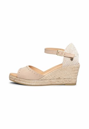 Sandalia cuña beige con pulsera en el tobillo, detalle de tacón tejido y pequeños tachuelas en la zona de los dedos.