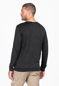 Camiseta de manga larga gris oscuro con cuello redondo, tejido texturizado y detalles cosidos en los puños y el dobladillo. Combinada con pantalones beige claros.