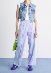 Jeansväst med en figurnära design, matchad med ljuslila träningsbyxor med ett subtilt mönster och gröna sidostråk. Accessoarer med en grön korgväska.