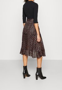 Czarny długi rękaw top połączony z plisowaną, wzorzystą spódnicą w ciemnych odcieniach, z falbaniastym dołem, noszony z czarnymi botkami na obcasie.