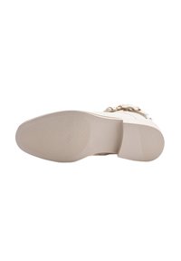 Suela de bota beige con almohadillas de agarre texturizadas en el talón y la planta, hebilla y correa visibles encima de la suela, aislada sobre fondo blanco.