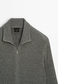 Maglione grigio lavorato a maglia con zip, caratterizzato da una texture a coste, un colletto alto e una zip in metallo. Presenta un'etichetta all'interno del colletto.