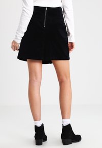 Mustat korduroypohjamaasi hame flared-muodolla, jossa on keskellä vetoketju takana. Yhdistetty valkoisen pitkänhihasen paidan ja mustien nilkkureiden kanssa.