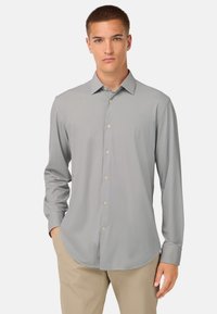 Maglietta a maniche lunghe grigio chiaro con un sottile motivo a quadretti, colletto button-down e patta frontale. Tessuto morbido e vestibilità regolare.