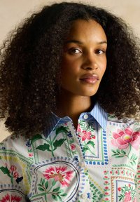 White button-up shirt with colorful floral and geometric patterns; light blue striped collar; cotton material.