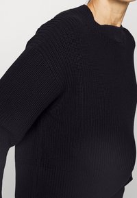 Pull noir tricoté avec un motif texturé, col rond et épaules tombantes, coupe décontractée et détails en côtes aux poignets.