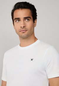 T-shirt bianco in cotone con scollatura rotonda e maniche corte. Presenta un piccolo logo ricamato blu navy sul lato sinistro del petto.