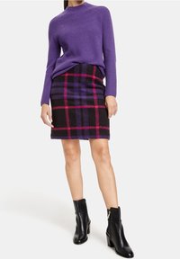 Maglione viola a coste, gonna nera con un motivo a quadri rosa e viola, e stivaletti neri alla caviglia con cerniera laterale.