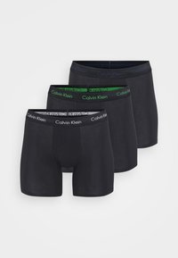 Drie paar zwarte boxershorts met contrasterende elastische taillebanden; één heeft een groene accenten, allemaal gelabeld met "Calvin Klein."
