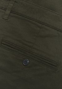 Olivově zelená tkanina s plochým předním designem, štíhlým střihem a jedním černým plastovým knoflíkem na pravé kapse s odpovídajícím prošíváním.