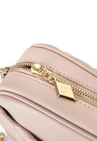 Borsa in pelle rosa chiaro con zip dorata, emblema impresso e texture trapuntata. Forma compatta con finitura liscia e cuciture dettagliate.