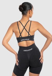 Sujetador deportivo negro y pantalones cortos de talle alto con un acabado texturizado. El sujetador presenta tirantes entrelazados y un logotipo en la cintura.