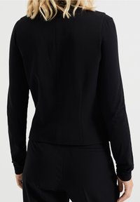 Svart långärmad topp med en figurnära design, jämn textur och hög krage. Har sömdetaljer på baksidan.