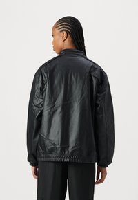 Veste en cuir noir avec une coupe décontractée, poignets côtelés et col montant. Présente une texture lisse et des détails subtils aux épaules.