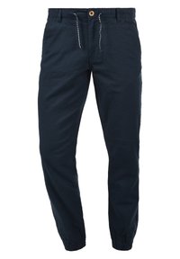 Marinblå bomullsbyxor med elastisk midja och justerbar dragsko. Har smalnade ben med elastiska muddar och sidofickor.