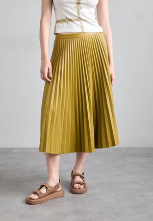 Pleated mustard-yellow midi skirt with a fitted waistband, textured fabric, and a smooth finish. Paired with brown strappy sandals.