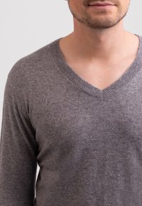 Szary sweter dzianinowy z dekoltem w serek, z długimi rękawami i miękką fakturą. Projekt jest prosty i zawiera ściągacz na dekolcie.