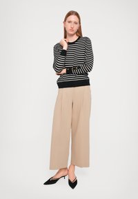Pull en tricot à rayures noir et blanc avec des poignets et un ourlet côtelés, associé à un pantalon large beige et des mules à bout pointu noires.