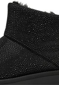 Nahaufnahme eines schwarzen Wildleder-Stiefelettes, das mit kleinen schwarzen Strasssteinen verziert ist und eine schwarze Gummisohle hat.