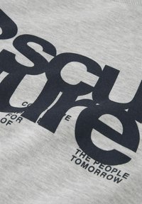 T-shirt en coton gris avec un grand texte imprimé bleu marine. Le design inclut des tailles de police variées et un texte supplémentaire sous le graphique principal.