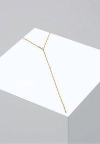 Collier délicat en or en forme de Y avec une fine chaîne, présenté sur une surface blanche inclinée sur un fond gris clair.