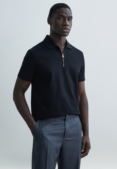 Black short-sleeve polo shirt with a zippered collar and gold hardware, paired with gray tailored trousers featuring a textured fabric.