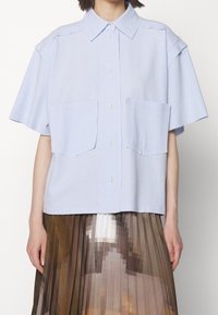 Jasnoniebieska koszula z krótkim rękawem na guziki, z fakturowanej tkaniny, z dwiema kieszeniami na przedzie i klasycznym kołnierzykiem.