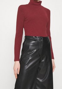 Rode geribbelde coltrui met lange mouwen, gecombineerd met hoge zwarte faux leren wijdse broek met een glanzende textuur.
