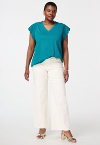 Haut teal à manches courtes avec des détails en dentelle sur les manches, associé à un pantalon large crème et des sandales à talons métalliques.