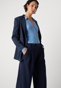 Navyblauer, gestreifter Blazer über einem hellblauen, gerippten Button-Up-Oberteil, kombiniert mit weit geschnittenen, navyblauen Hosen; besitzt Taschen und einen lässigen Schnitt.