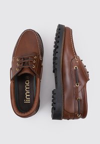 Zapatos de cuero marrón con puntera redonda, suela de goma, diseño de cordones, costuras en contraste y acentos laterales. La textura parece suave con un detalle menor.