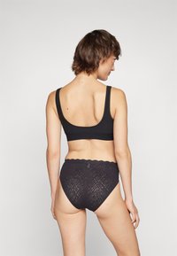 Brassière noire à large bretelles et dos échancré, accompagnée de culottes en dentelle noires taille haute mettant en valeur un motif géométrique et des bords festonnés.