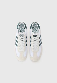 White athletic shoes with green stripes, suede toe cap, and textured insole featuring the Adidas logo. Laces are light gray.