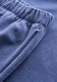 Blue cotton sweatpants feature a gathered waistband and a smooth texture with a side slit pocket, emphasizing comfort and ease of movement.
