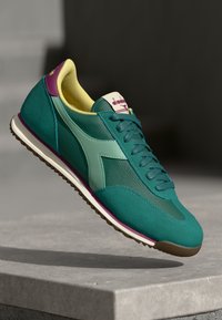 Teal sportieve schoen van mesh en suede materialen. Bevat een mintgroene accent, paarse hiel, gele voering en witte rubberen zool.
