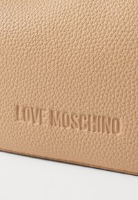 Borsa a tracolla in pelle beige con un texture e logo "LOVE MOSCHINO" impressi, caratterizzata da una finitura liscia e un sottile motivo di grana dettagliato.