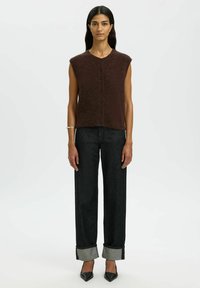 Kasztanowy bezrękawnik dzianinowy z okrągłym dekoltem i sześcioma ciemnymi guzikami, połączony z wysokim stanem ciemnych dżinsów z mankietami.