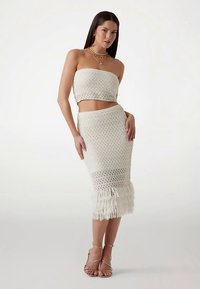 White knitted two-piece set featuring a strapless crop top and a knee-length skirt with fringe detailing at the hem.