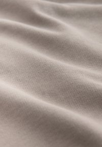 Tela beige suave con una textura finamente acanalada y pliegues suaves que crean sombras y reflejos sutiles.