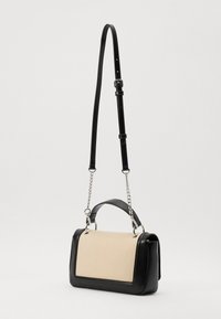 Black leather bag with a beige textured front, featuring a top handle, an adjustable strap, and chain accents on the sides.